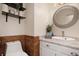 Well-lit half bath with modern fixtures, elegant round mirror, and tiled accent wall at 15393 E Louisiana Ave, Aurora, CO 80017