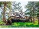 Charming home featuring a large deck and stairs surrounded by lush greenery and mature trees at 24999 Grandview Ave, Golden, CO 80401