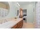Bathroom featuring a wooden vanity with dual sinks, a large oval mirror, and a shower with tiled walls at 7071 Turweston Ln, Castle Pines, CO 80108