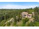 Aerial view showing the tile roof home's positioning on a rocky hill with large trees and a partial deck at 857 Pawnee Trl, Castle Rock, CO 80108