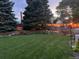 Expansive backyard with a manicured lawn, raised garden beds, mature trees, and charming string lights at 7946 S Pennsylvania Ct, Littleton, CO 80122