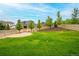 Spacious backyard featuring lush green grass, trees, and a sand pit surrounded by a wooden fence at 4145 Manorbrier Cir, Castle Rock, CO 80104