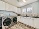 A modern laundry room has a front-load washer and dryer with white cabinets and neutral mosaic backsplash at 18971 E Pinewood Dr, Aurora, CO 80016