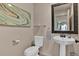 Well-lit half bathroom with a pedestal sink, decorative mirror, and modern fixtures at 16453 Homestead Ct, Parker, CO 80134