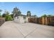 Wide driveway leading to the side of a home with a wood fence, lush trees, and green lawn at 1260 Hoyt St, Lakewood, CO 80215