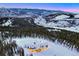 Stunning aerial view of a mountain estate with lights glowing against the snowy landscape and mountain backdrop at 250 Sallie Barber Rd, Breckenridge, CO 80424