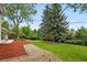 Backyard showing a lawn, rock pathway, and mulch area, surrounded by mature trees and lush greenery at 11880 W 30Th Pl, Lakewood, CO 80215
