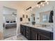Elegant bathroom featuring double sinks with granite countertops and dark wood cabinetry, adjacent to bedroom at 12578 Hudson Ct, Thornton, CO 80241