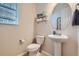 Bright powder room featuring a pedestal sink, toilet, and decorative shelving with a window for natural light at 12578 Hudson Ct, Thornton, CO 80241