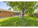 View of the brick home backyard with a covered patio and lush green lawn with mature trees at 649 Nucla Way, Aurora, CO 80011