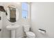 Bright powder bathroom with a pedestal sink, toilet and window, accentuated with a round mirror and a basketball hoop at 5388 Routt St # B, Arvada, CO 80002