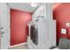 Functional laundry room with white washer and dryer, built-in cabinets, and bright red wall at 13664 Linden Ct, Thornton, CO 80602