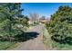 View of a gravel driveway leading to a quaint home, framed by mature trees and a well-maintained yard at 7409 S County Road 157, Strasburg, CO 80136