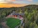 Aerial view of a modern home with a large yard and surrounding forest at dusk at 34089 Woodland Dr, Evergreen, CO 80439
