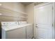 Efficient laundry room with white washer, dryer, shelving, and door at 6812 Indian Paintbrush St, Frederick, CO 80530
