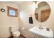 Powder room featuring a pedestal sink, toilet, round mirror, and window at 18750 Spring Valley Rd, Monument, CO 80132