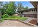 A beautiful backyard featuring mature trees, a brick house, a stone patio, and lush greenery at 2717 S Langley Ct, Denver, CO 80210