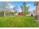 Spacious backyard featuring a green lawn, red storage shed, and a cozy greenhouse at 2210 Miller St, Lakewood, CO 80215