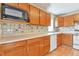 Traditional kitchen featuring wooden cabinetry, white appliances, and decorative tile backsplash at 13581 Sable Blvd, Brighton, CO 80601