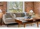 Comfortable living room featuring a modern sofa, brick wall, and bright natural lighting at 624 E 18Th Ave # 3, Denver, CO 80203