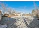 Wide shot of a large gravel backyard, with a blue sky overhead and mature trees surrounding at 1934 Macon St, Aurora, CO 80010