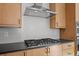 Close-up of a modern gas range with a stainless steel hood and a bright white backsplash, mounted over gray counter at 5584 Moosehead Cir, Longmont, CO 80504