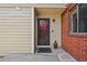 Front door with black screen door, doormat, and gnome is framed by brick and beige siding at 7474 E Arkansas Ave # 13-02, Denver, CO 80231