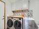 Modern laundry room with stainless steel washer and dryer, storage cabinets, and mosaic tile backsplash at 13517 Clayton Ct, Thornton, CO 80241