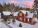 Charming red home with snow-covered roof, adjacent guest house, and snowy yard with mature trees at dusk at 102 S High St, Breckenridge, CO 80424