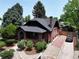 Aerial view of brick home with a dark roof, green trees and landscaping, gravel driveway, and a fenced yard at 2636 N Glencoe St, Denver, CO 80207