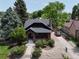 Aerial view of brick home with a dark roof, green trees and landscaping, gravel driveway, and a fenced yard at 2636 N Glencoe St, Denver, CO 80207