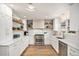 Bright white kitchen with stainless steel appliances, light countertops, floating shelves, and modern fixtures at 5121 W Plymouth Dr, Littleton, CO 80128