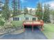 Back of a light green home with a dark red balcony, surrounded by lush greenery and a dark driveway at 8473 Gray Fox Dr, Evergreen, CO 80439