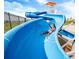 A person enjoying a thrilling ride down the community's vibrant blue water slide on a sunny day at 27460 E Cedar Pl, Aurora, CO 80018