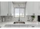 Kitchen sink with white cabinets, modern faucet, and marble-style backsplash under window at 3296 S Bryant St, Englewood, CO 80110
