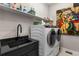 Well-equipped laundry room featuring sleek black countertops, a modern sink, and a high-end washer and dryer at 741 Green Mountain Dr, Erie, CO 80516
