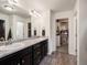Bathroom featuring double sinks, dark cabinets, granite countertop, and walk-in closet access at 5358 Ventura St, Denver, CO 80249