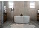 Bright bathroom featuring a modern soaking tub, herringbone tile accent wall, and wood-look tile flooring at 27608 E Ottawa Ave, Aurora, CO 80016