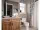 Well-lit bathroom features a wooden vanity, a toilet, and a shower with patterned curtains at 27608 E Ottawa Ave, Aurora, CO 80016