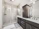 Elegant bathroom with glass shower, dark cabinets, dual sinks, and bright lighting at 15747 Willow Way, Thornton, CO 80602