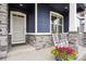 Close-up of charming blue home's front porch with grey door, stone columns, and rocking chairs at 8888 Falcon St, Longmont, CO 80504