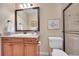 Bathroom featuring granite countertop, wood cabinets, framed mirror, and tiled shower with glass doors at 9351 Viaggio Way, Highlands Ranch, CO 80126