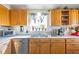 Well-lit kitchen with oak cabinets, stainless steel dishwasher, and window with plants at 5106 Eagle Ct, Denver, CO 80239