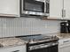 Close-up of the updated kitchen featuring stainless steel appliances, herringbone backsplash, and granite countertops at 14823 W 70Th Dr # A, Arvada, CO 80007
