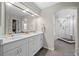 Bright bathroom featuring dual sinks, white cabinetry, and a glass-enclosed shower with gray tile flooring at 5272 W Capri Pl, Littleton, CO 80123