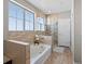 Bright bathroom featuring a soaking tub, a glass-enclosed shower, and neutral tile surround at 14077 Indianfield Ct, Hudson, CO 80642