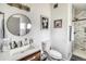 Bathroom featuring a round mirror, wood vanity, sink, toilet, framed art, and shower with marble tile at 450 Yukon St, Lakewood, CO 80226