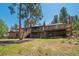 Back exterior of brick home with a wooden deck and railing is surrounded by mature trees at 7845 Armadillo Trl, Evergreen, CO 80439