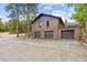 Brick house showcasing a three-car garage and upper deck, surrounded by mature trees and natural beauty at 7845 Armadillo Trl, Evergreen, CO 80439