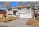 Split-level home featuring neutral siding, a red front door, attached garage, and a well-maintained front yard at 12843 W Jewell Cir, Lakewood, CO 80228